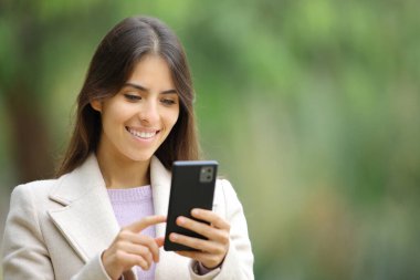 Happy woman in winter using smart phone in a green park