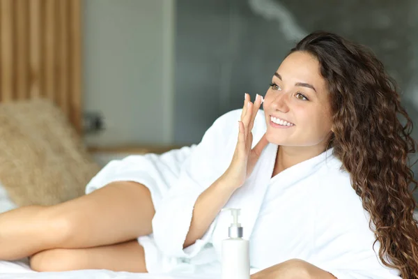 幸せな女性は自宅でベッドの上に保湿剤を適用顔の皮膚を水和物 — ストック写真