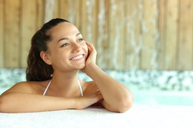 Spa havuzunda mutlu bir kadın yan bakıyor.