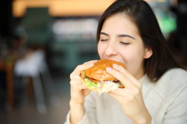 Restoranda hamburger yiyen mutlu bir kadın.
