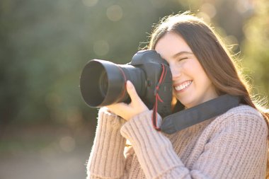 Mutlu kadın, kışın parkta profesyonel kamerayla fotoğraf çekiyor.