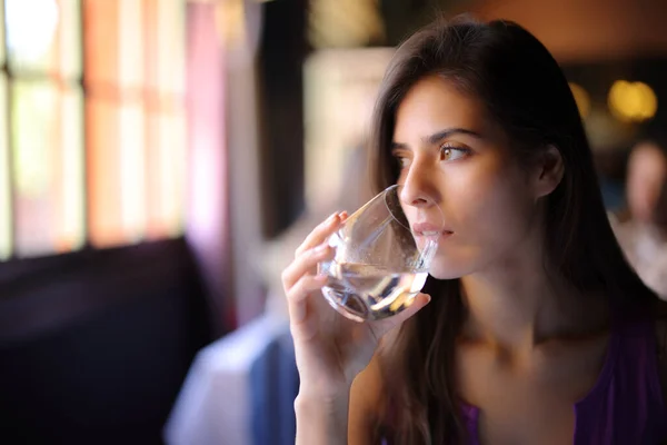 一个严肃的女人坐在餐厅边看边喝水 — 图库照片