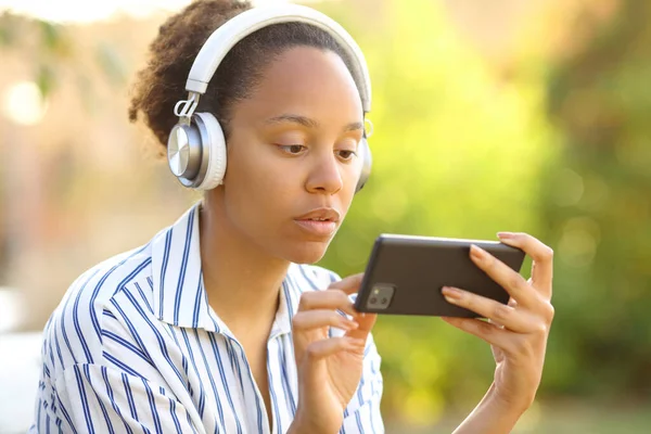 Poważna Czarna Kobieta Słuchawce Ogląda Filmy Przez Telefon Parku — Zdjęcie stockowe