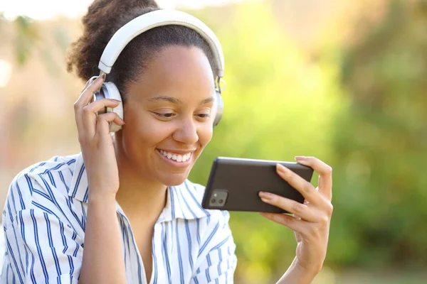 Счастливая Чернокожая Женщина Наушниках Смотрит Видео Телефону Парке — стоковое фото