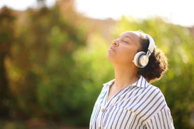 Siyah kadın parkta kulaklık takarak meditasyon yapıyor.