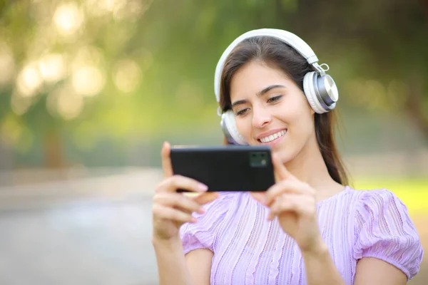 快乐的女人 带着耳机在公园里看手机视频 — 图库照片