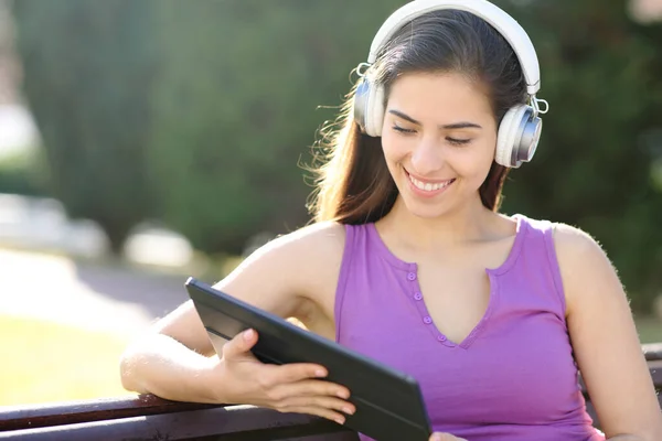 公園に座ってヘッドフォンでタブレット上のメディアを見て幸せな女性 — ストック写真
