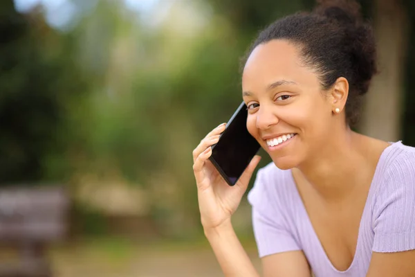 Stock image Happy black woman calling on phone looking at you in a park