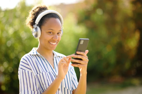 Szczęśliwy Czarny Kobieta Nosi Słuchawki Trzyma Smartfon Pozowanie Patrząc Aparat — Zdjęcie stockowe
