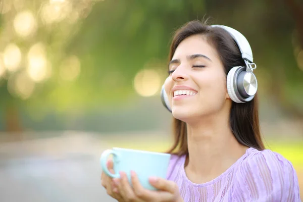 Happy Woman Wearing Headphone Listening Music Holding Coffee Mug Park — Stock Photo, Image