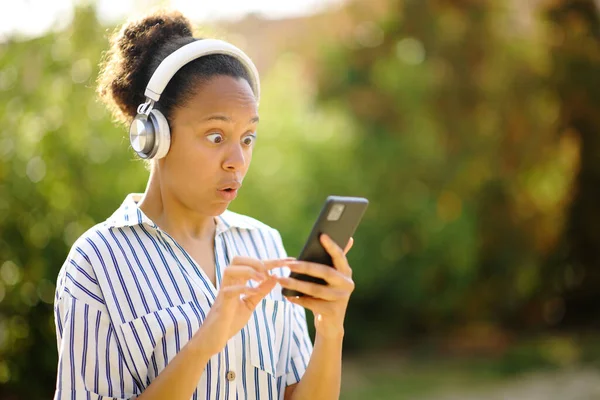 Zaskoczony Czarny Kobieta Noszenie Słuchawki Słuchanie Muzyki Telefonie Parku — Zdjęcie stockowe