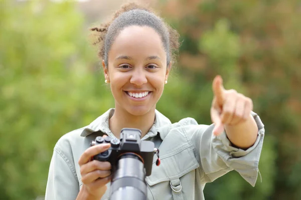 stock image Front view portrait of a black photographer pointing at camera holding mirrorless camera in a park