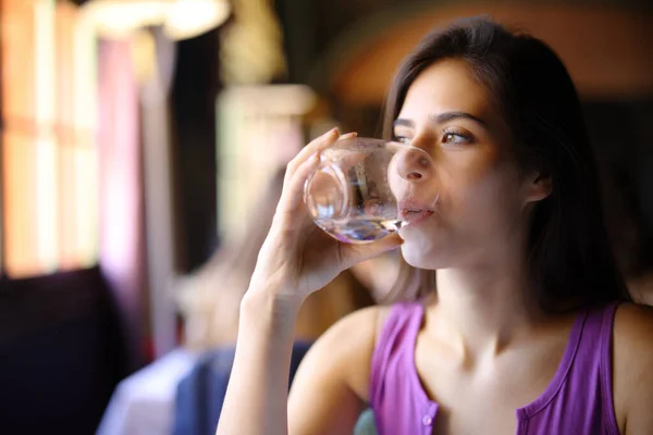 坐在餐馆内部用玻璃杯喝水的女人 — 图库照片