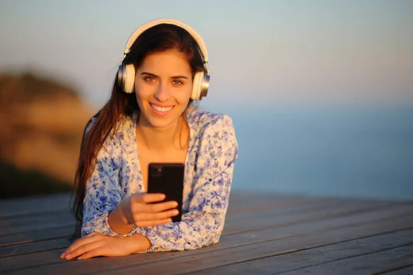 一个戴着耳机 在海滩上听音乐 看着你的快乐女人的正面肖像 — 图库照片