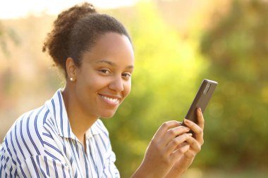 Parkta sana bakan akıllı telefonu kullanan mutlu siyah kadın.