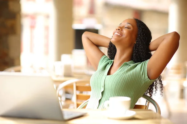 Black woman with laptop relaxing in a bar terrace