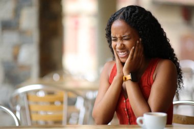 Black woman suffering tmj and complaining in a restaurant terrace clipart