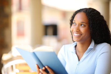 Kahvehanenin terasında elinde kağıt kitapla duran mutlu siyah okuyucu.