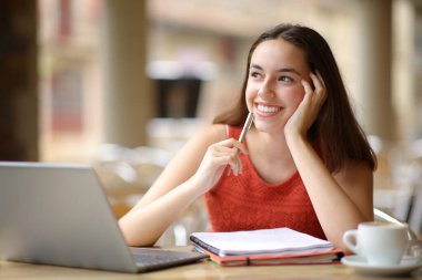 Dizüstü bilgisayarı ve dizüstü bilgisayarı olan mutlu öğrenci bir restoranın terasına bakıyor.