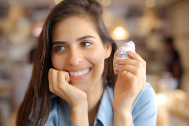 Güzel gülüşlü mutlu bir kadın bar içinde kruvasan tutuyor.