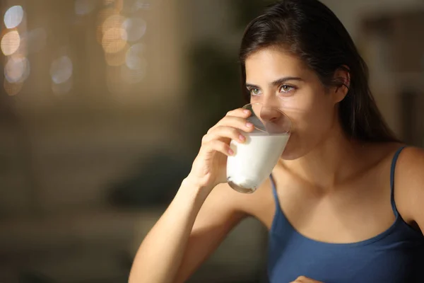Serious woman drinking milk looking away at home in the night