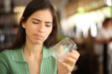 Disappointed woman looking at empty glass in a bar interior clipart