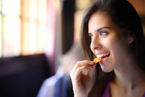 Happy restaurant customer eats chips and looks away through a window