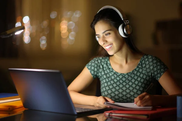 自宅でラップトップとヘッドフォンで学ぶ夜の幸せな学生 — ストック写真