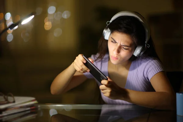 自宅で夜に電話でオンラインゲームをプレイする女性 — ストック写真