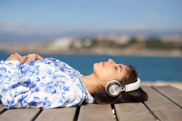 一名带着耳机听录音的轻松女子躺在海滨的侧视图画像 — 图库照片
