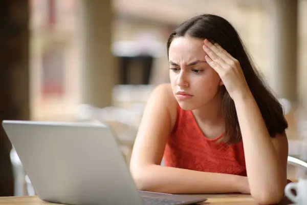 Worried woman checking laptop content sitting in a restaurant terrace