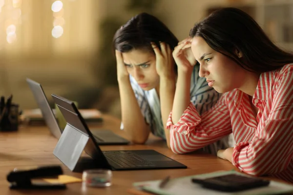 Worried tele workers checking bad news on tablet in the night at home