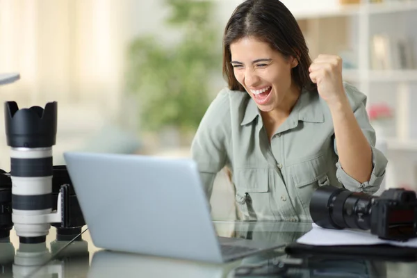 Excited photographer celebrating good result watching laptop content at home