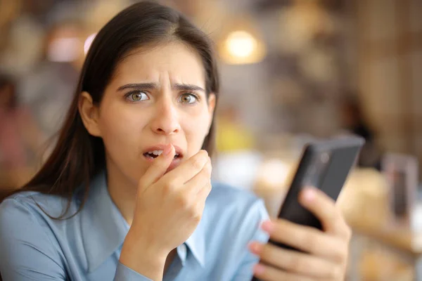 Terrified woman holding phone in a bar looking at camera