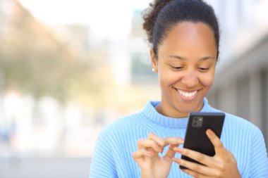 Sokakta gülümseyen akıllı telefonu kullanan mutlu bir kadının ön görüntüsü.