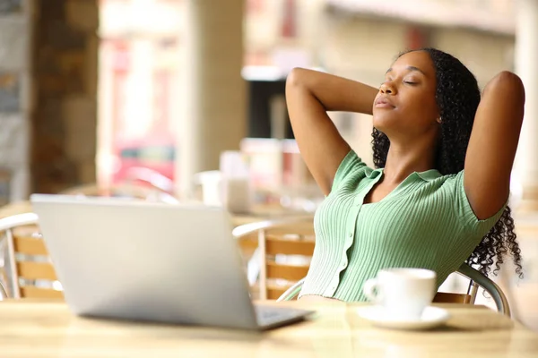 Black woman with laptop resting and relaxing in a restaurant terrace