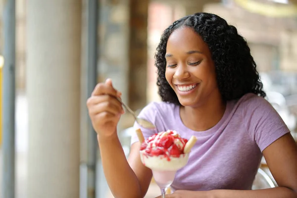 Happy black woman eating ice cream in a restaurant terrace