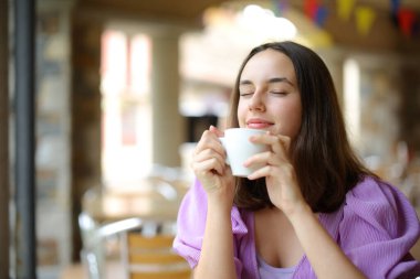 Rahatlamış bir kadın restoranın terasında kahve kokusu alıyor.