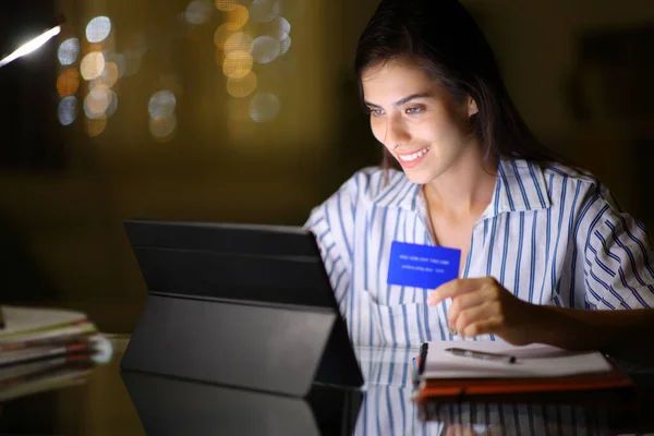 Happy student in the night buying online with tablet and credit card at home