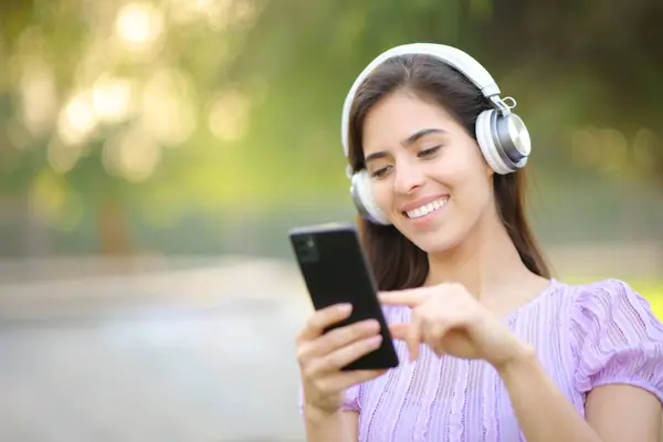 公園でヘッドフォンとスマートフォンを使用して音楽を聴く幸せな女性 — ストック写真