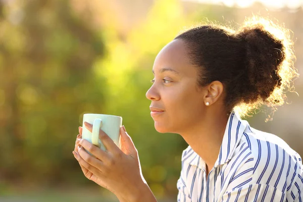 Side view portrait of a black woman contemplating holding coffee cup in a park