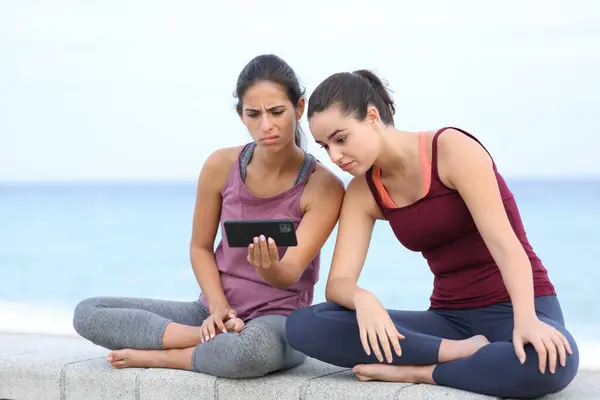 Frustrated yogis watching difficult yoga tutorial online on phone on the beach