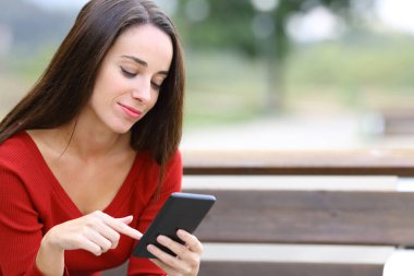 Kırmızılı kadın parkta bankta oturan akıllı telefonu kontrol ediyor.