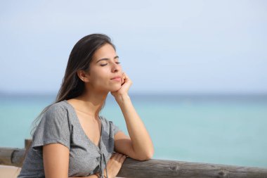 Woman resting on the beach relaxing alone leaning on a wooden railing clipart