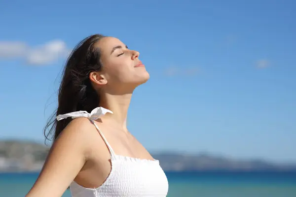 Profile of a relaxed woman in white dress breathing fresh air on the beach a summer sunny day