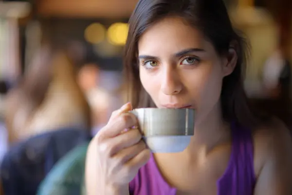Beautiful woman drinking coffee looking at you in a shop