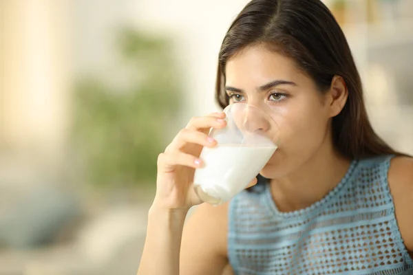 Serious woman drinking milk from transparent glass at home