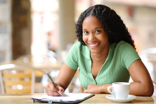 快乐的黑人女人在酒吧的阳台上填写表格看着你 — 图库照片
