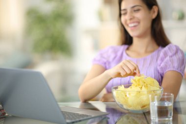 Happy woman watching movie on laptop eating potato chips at home clipart