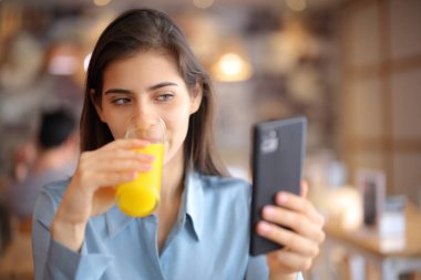 Portakal suyu içen bir kadın barın içinde telefona bakıyor.